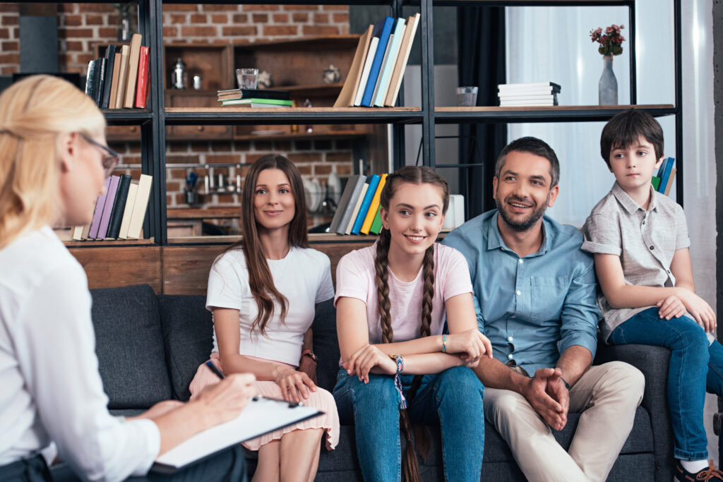 Smiling Family On Therapy Session By Female Counselor Writing In
